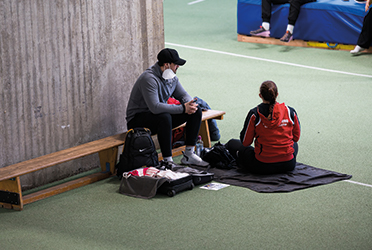 Auf dem Foto sieht man einen Sportler und eine Sportlerin in einer Trainingshalle sitzen. Der Sportler trägt eine Schutzmaske. (verweist auf: COVID-19 im Spitzensport – Eine multizentrische Kohorten-Studie)