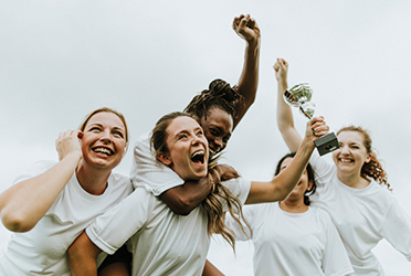 Das Bild zeigt eine Gruppe Frauen, die jubelt. Eine der Frauen streckt einen Pokal in die Höhe. (verweist auf: Inter­nationaler Welt­frauen­tag: Frauen im Sport)