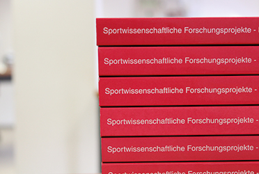 Auf dem Bild ist ein Bücherstapel zu sehen. Auf dem Buchrücken steht &#034;Sportwissenschaftliche Forschungsprojekte&#034;. Die Bücher sind rot. (verweist auf: BISp-Forschungsprojekte mit COVID-19-Bezug – ein erster Überblick)