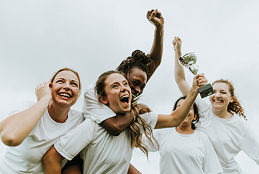 Das Bild zeigt eine Gruppe Frauen, die jubelt. Eine der Frauen streckt einen Pokal in die Höhe.